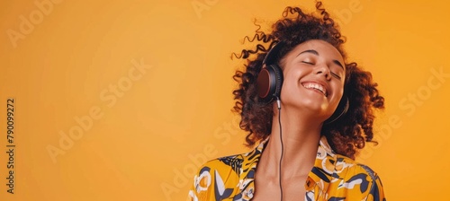 A curly haired young woman listening to music on an orange background photo