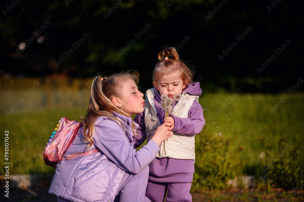Two siblings share a tender moment in golden sunlight as they blow dandelion seeds, surrounded by the warmth of a spring evening Two siblings share a tender moment in golden sunlight as they blow dandelion seeds, surrounded by the warmth of a spring evening