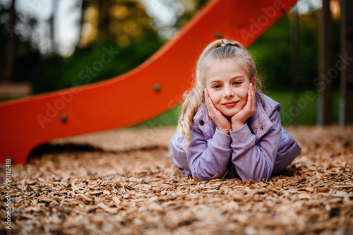 Φωτογραφία A young girl rests her head in her hands on the playground woodchips, her though