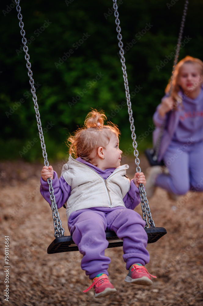 A toddler's fascination is captured mid-swing, her gaze fixed on her older sister, a snapshot of innocent wonder and sibling bonds. A toddler's fascination is captured mid-swing, her gaze fixed on her older sister, a snapshot of innocent wonder and sibling bonds.