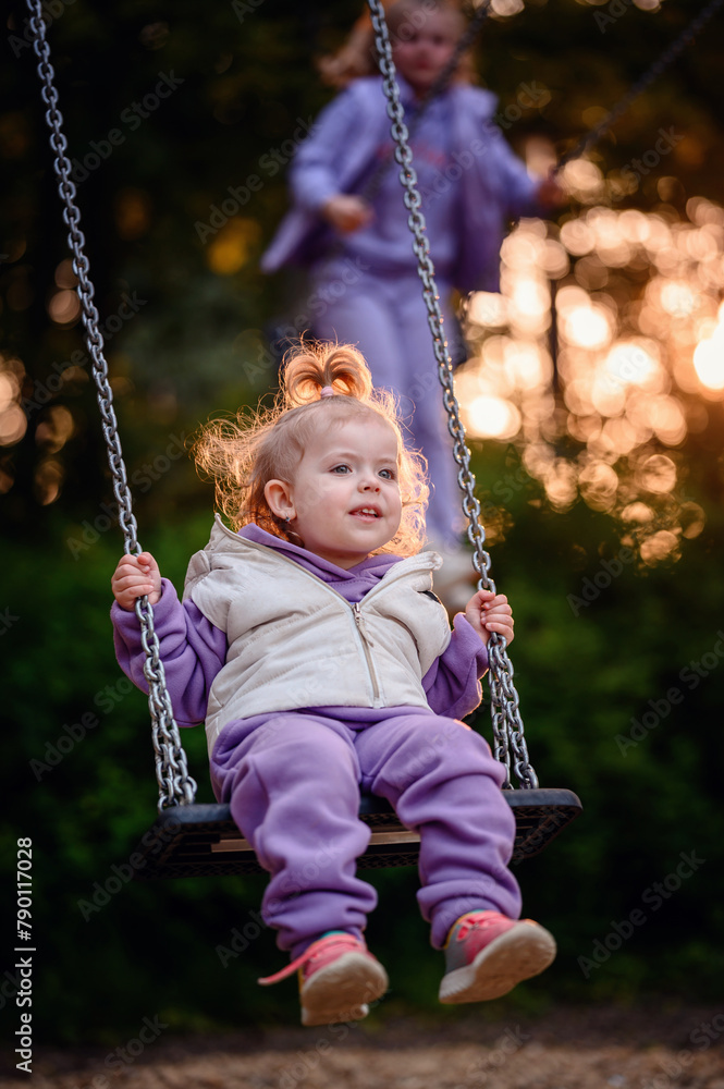 A toddler's fascination is captured mid-swing, her gaze fixed on her older sister, a snapshot of innocent wonder and sibling bonds. A toddler's fascination is captured mid-swing, her gaze fixed on her older sister, a snapshot of innocent wonder and sibling bonds.