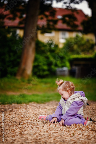 A curious toddler in a purple outfit sits among wood chips  fascinated by the textures  illustrating the simple joys and tactile experiences of outdoor play