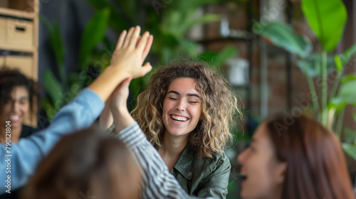 Surrounded by colleagues offering congratulations, a white woman shares a high-five in her office, her expression one of elation and excitement, her beaming smile radiating happine