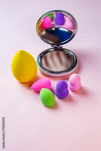 Colorful blender makeup sponges blending puff set and round shaped mirror on a pink background with copy space. beauty concept vertical photo