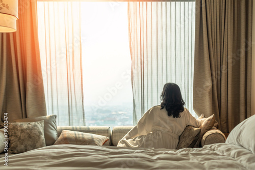 Hotel relaxation on lazy day with Asian woman waking up from good sleep on bed in weekend morning resting in comfort bedroom looking toward city view, having happy, work-life quality balance lifestyle © Chinnapong