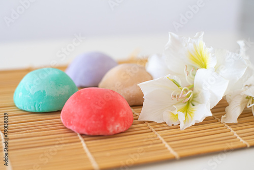 Four mochi different colors on bamboo makisu with flowers on light background. Japanese traditional frozen dessert mochi. ice cream with dough of sticky rice. fresh delicious appetizer. asian cuisine