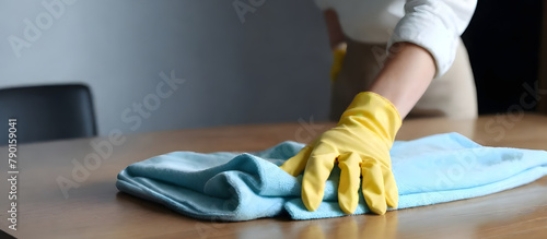 A person is wiping a wooden table with a cloth to clean and remove dust and dirt
