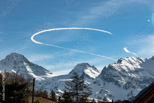 Curved Chemtrail above snowy mountains Swiss Alps Switzerland