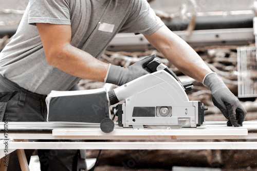 A young man is sawing a board with an electric saw.