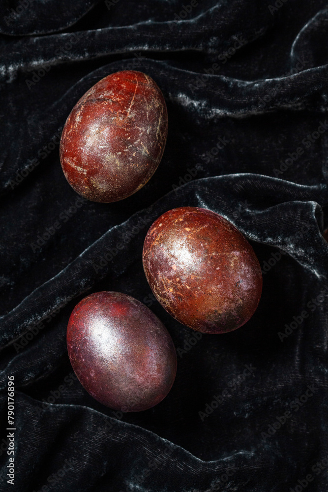 Eggs stained with wine and covered with mother-of-pearl on a dark velvet background. Easter concept.