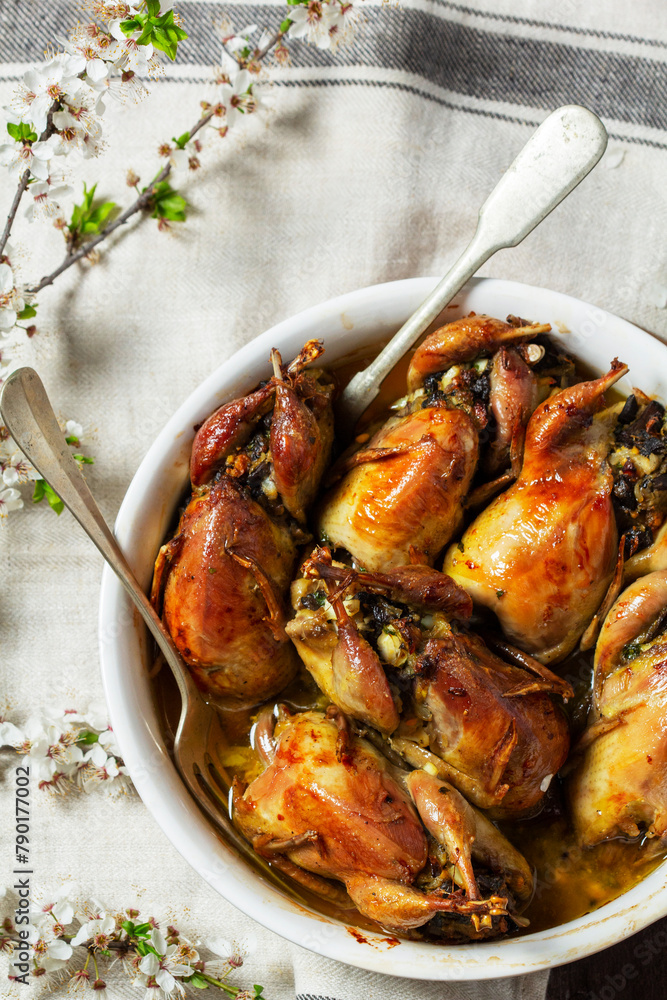 Baked quail stuffed with mushrooms, eggs and bread in a ceramic form on a wooden table.