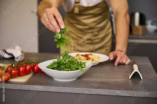 Close-up chef hands holding fresh arugula leaves, garnishing meal, cooking Italian spaghetti in the home kitchen.