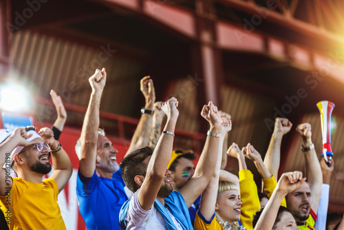 Closeup of hands in the air. Sport fans cheering at the game on stadium. Wearing yellow and blue colors to support their team. Celebrating with flags and scarfs.