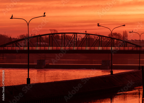 czerwony wschód słońca nad rzeką z sylwetką mostu i ptakami na latarniach