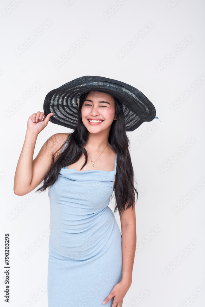 Smiling young Asian woman in baby blue dress wearing a large black straw hat isolated on white Smiling young Asian woman in baby blue dress wearing a large black straw hat isolated on white