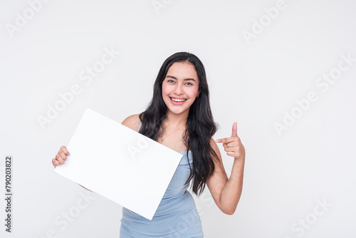 Young woman in baby blue dress enthusiastically pointing to a blank sign, isolated on white