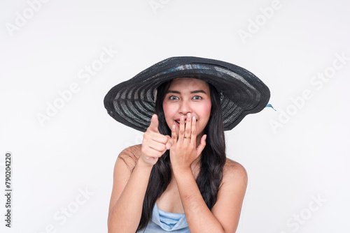 A cheerful Asian woman wearing a baby blue dress and a large black straw hat, Recognizing someone familiar, expressing suprise and joy, isolated on a white background.