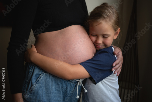 Little cute daughter hugging pregnant mother at home