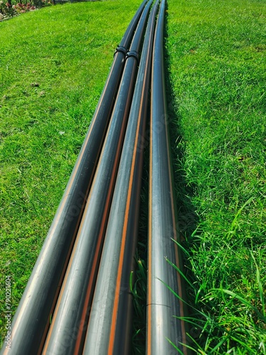 Close-up of four black plastic pipes neatly arranged on lush green grass field under bright sunlight, showcasing contrast between man-made objects and natural environment.