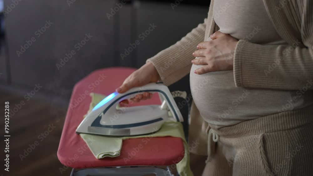 Closeup. An unrecognizable pregnant woman uses a steam iron to iron