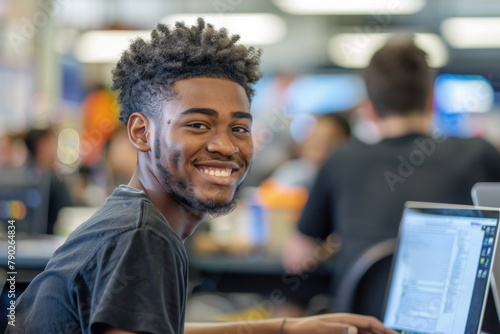 A young African American man smiling while working on his laptop in a vibrant and lively university setting