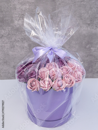 A bouquet of roses in a round box is packed in a transparent film and tied with a bow