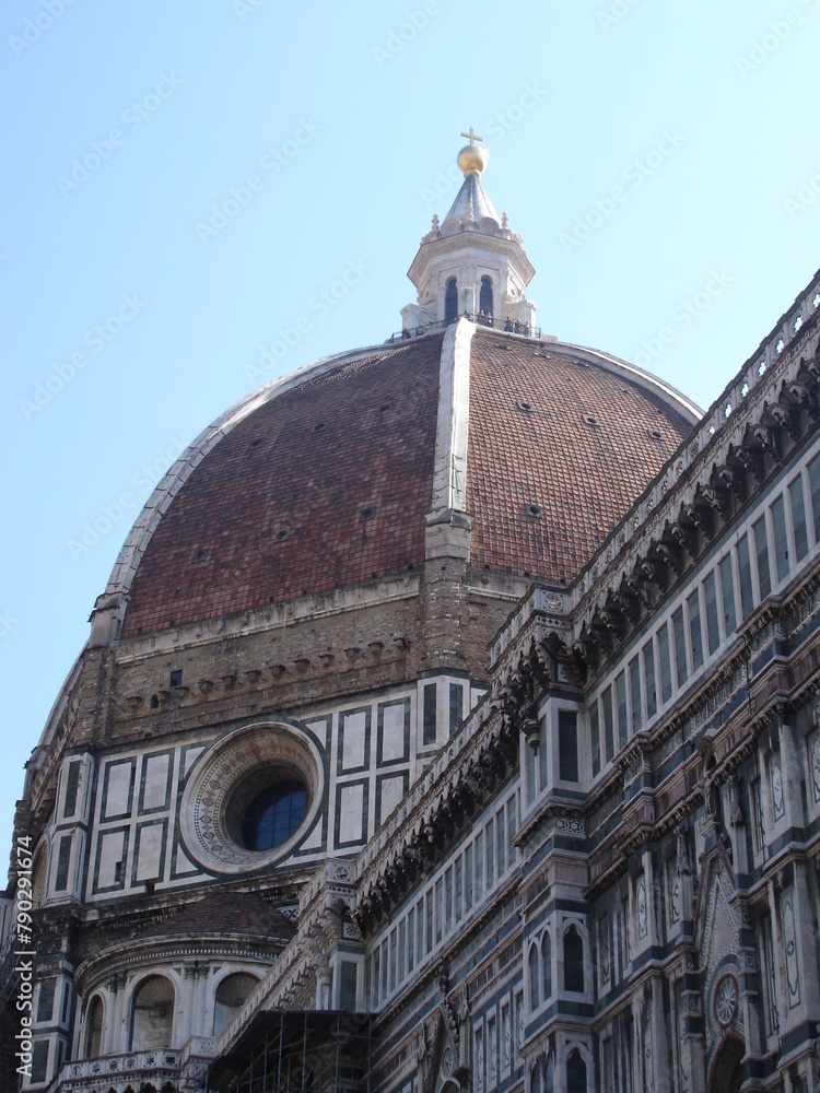 Ground-level view of the domed roof of the Santa Maria del Fiore duomo in Florence, Italy set against a light blue sky.