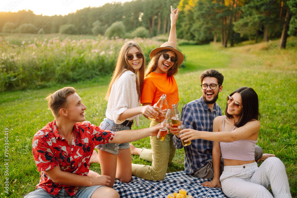 © maxbelchenko - Group of young people having fun while drinking beer at picnic party. Friends enjoy sunny day. Vacation, weekend, friendship or holliday concept.
