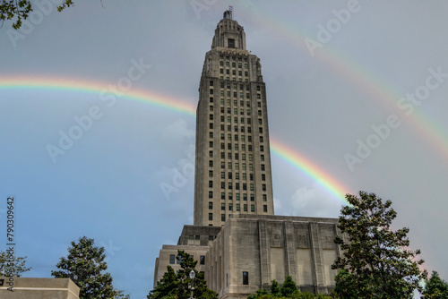 The Louisiana State Capitol building with lush green trees, blue sky, clouds and a rainbow in Baton Rouge Louisiana USA