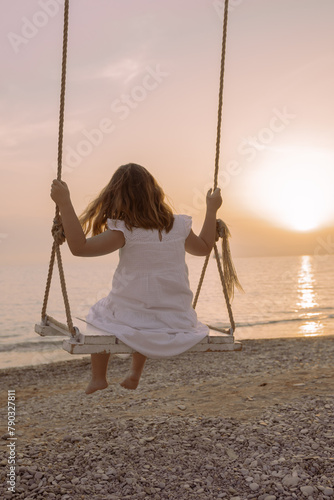 a child at sunset swings on a swing over the sea while traveling on vacation