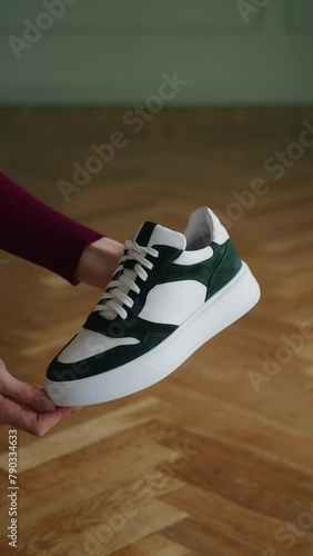 Hand holding a green and white sneaker with wooden floor background. Close-up product shot for shoe advertising with copy space, design for sports footwear marketing