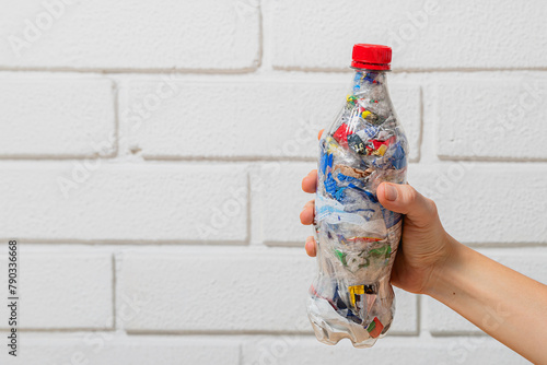 hand holding one eco brick PET bottle stuffed with plastic waste with white brick wall