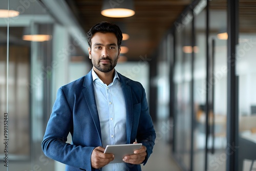 Selbstbewusster indischer Geschäftsmann, Vielbeschäftigter Geschäftsmann steht mit digitalem Tablet in den Flur, modernes Büro