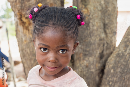 african girl with braids and beads, in front of a tree in the township