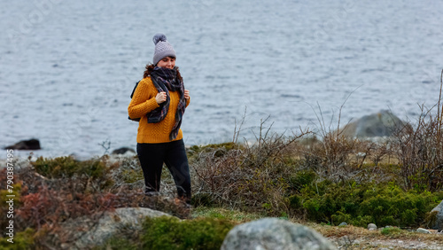 A mature woman in a yellow sweater and skarf walking by coast path, embodying the calm of a solitary coastal walk. Concept: meditation, solitude, sea exploration photo