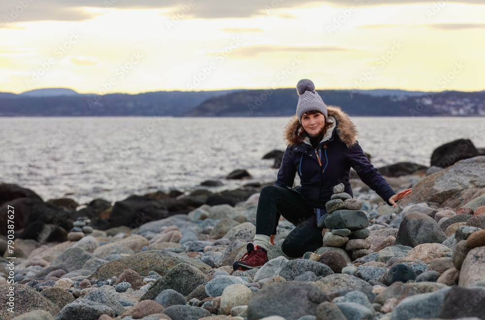 A focused woman practices the art of rock balancing on a seashore at winter dusk, creating a harmonious structure that symbolizes balance and tranquility. Concept: mindfulness, harmony, creativity A focused woman practices the art of rock balancing on a seashore at winter dusk, creating a harmonious structure that symbolizes balance and tranquility. Concept: mindfulness, harmony, creativity