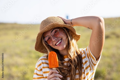 Canvas Print Attractive young woman eating a orange popsicle looking at the camera on summer