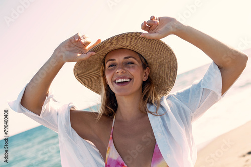 Beautiful woman in bikini posing at camera with a straw hat at the beach