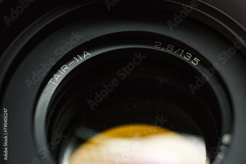 Detailed view of TAIR-11A camera lens engraving, with focal length and aperture value, precision instrument for photography, against a blurred dark background.