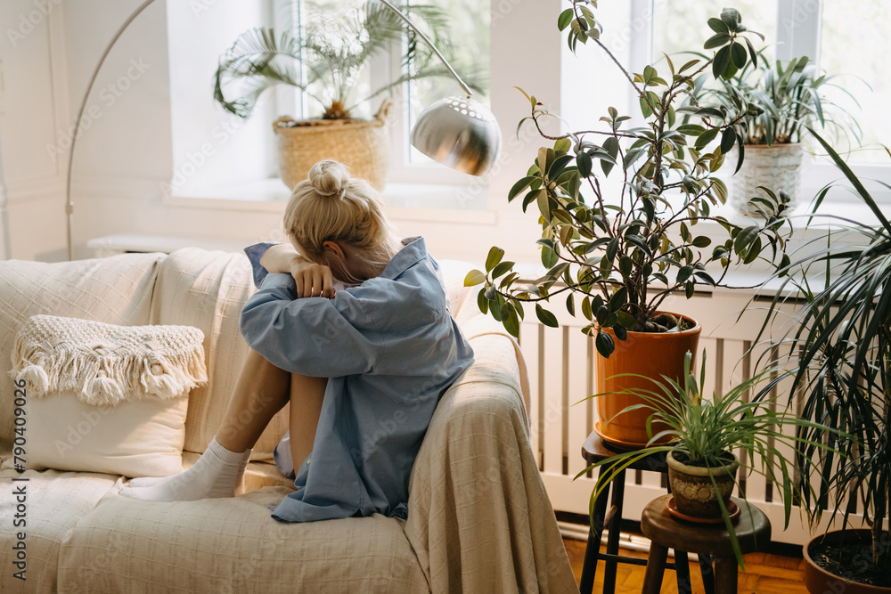 Sad lonely woman sitting on sofa at home in a full of natural light room. Sad lonely woman sitting on sofa at home in a full of natural light room.