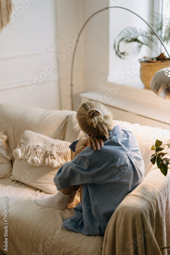 Woman enjoys morning light at home, sitting on sofa, looking away through the window.