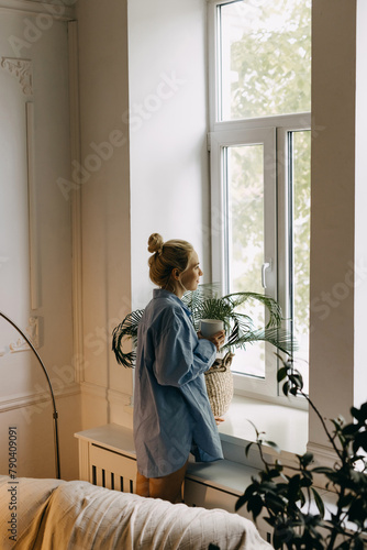 Blonde woman with a cup of tea or coffee in the morning at home, looking through the window.
