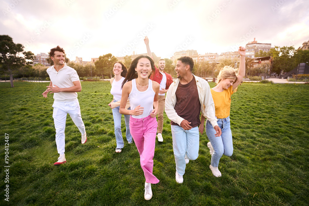 Fototapeta premium Group of young people in community celebrating and having fun outdoors at park. They laugh and run to the camera. Multiethnic group of friends together. Gathering unity in summer mood Diverse students