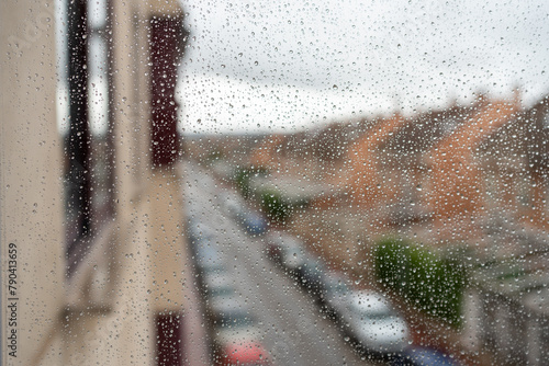 Home window filled with raindrops. Out of focus image of a city street in the rain.