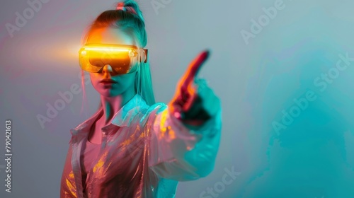 Confident young woman in led modern vr goggles pointing finger while experiencing immersive virtual world on blue background