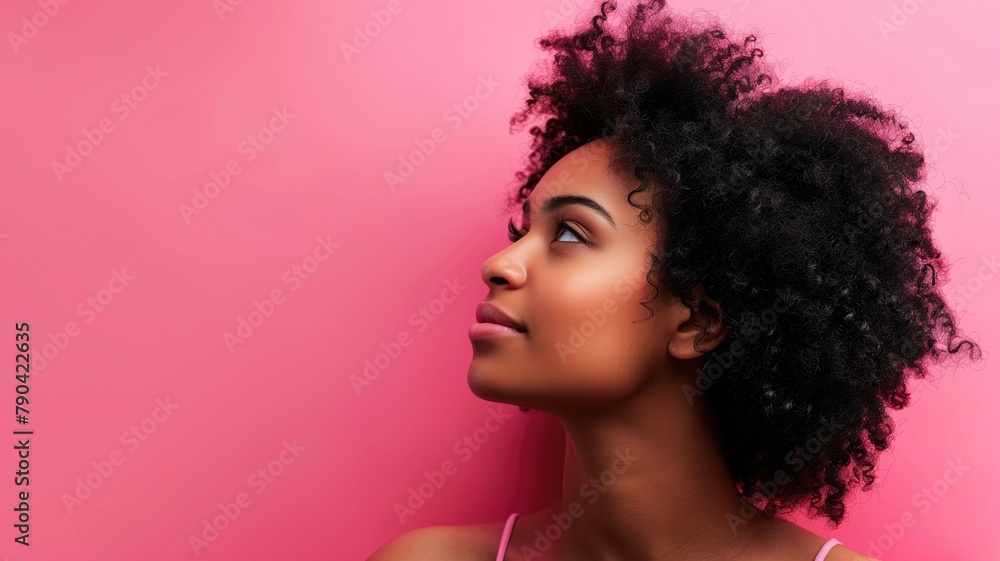 Young African woman with curly hair against pink background, looking upwards Young African woman with curly hair against pink background, looking upwards