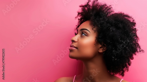 Young African woman with curly hair against pink background  looking upwards