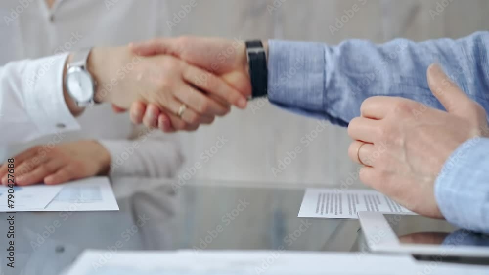 Business people shaking hands over contract agreement and financial papers at the glass table. Professional handshake, close up Business people shaking hands over contract agreement and financial papers at the glass table. Professional handshake, close up
