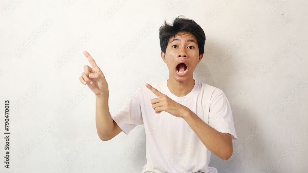 young asian man poses surprised while pointing upwards on a white background young asian man poses surprised while pointing upwards on a white background