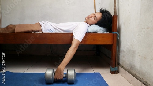 young Asian man sleeping on the bed with his dumbbells. don't have time to exercise. lazy to exercise